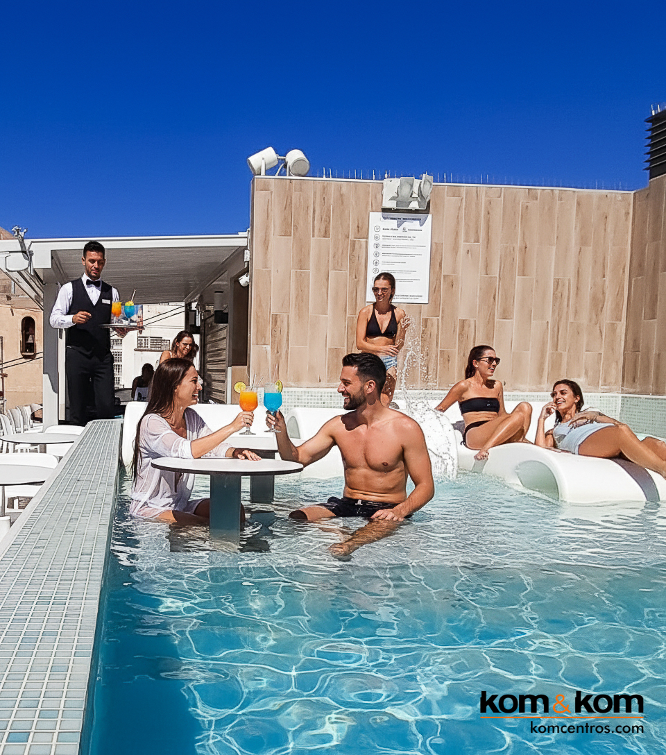 Ambiente de piscina en terraza de azotea. Personas ba&ntilde;&aacute;ndose, pareja con c&oacute;cteles en mesa flotante y camarero sirviendo bebidas. Lujo y relax en dise&ntilde;o de exteriores.
